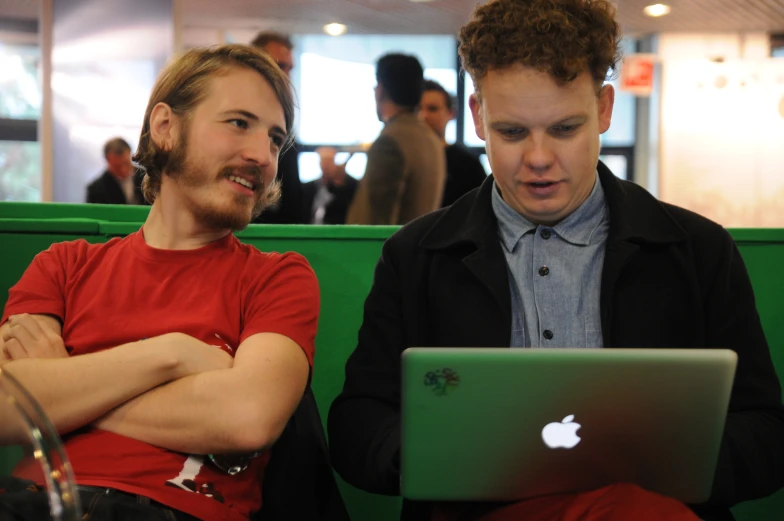 two people sitting in a booth, one on a laptop and the other working