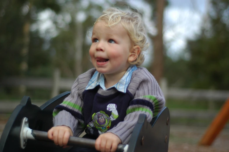 a little blonde toddler smiles while riding on a toy