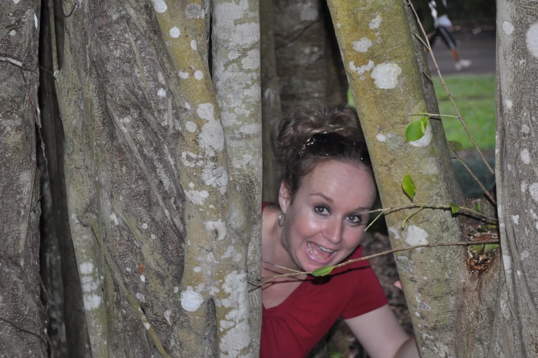 a young woman is peeking out from behind two trees