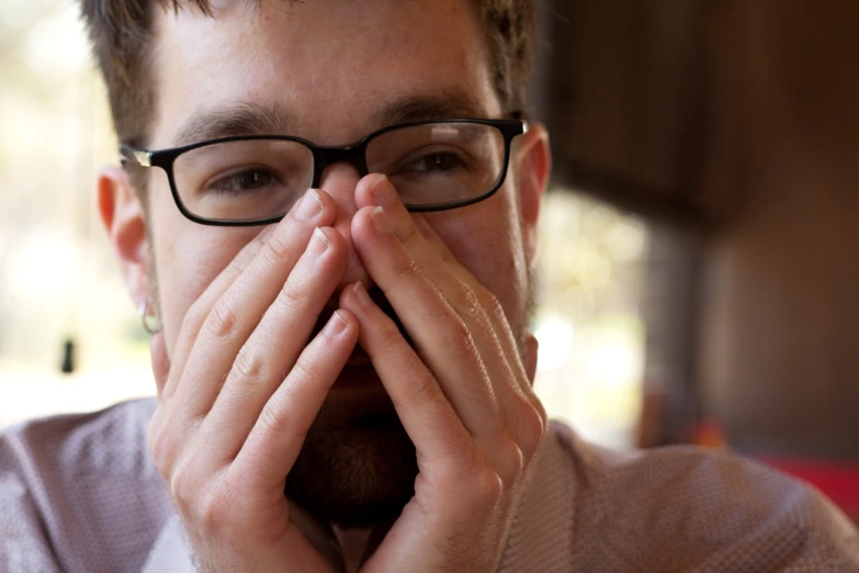 a man wearing glasses covering his face with his hands