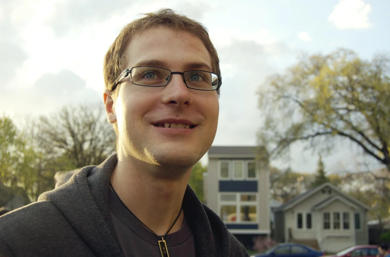 a man with glasses and a house in the background