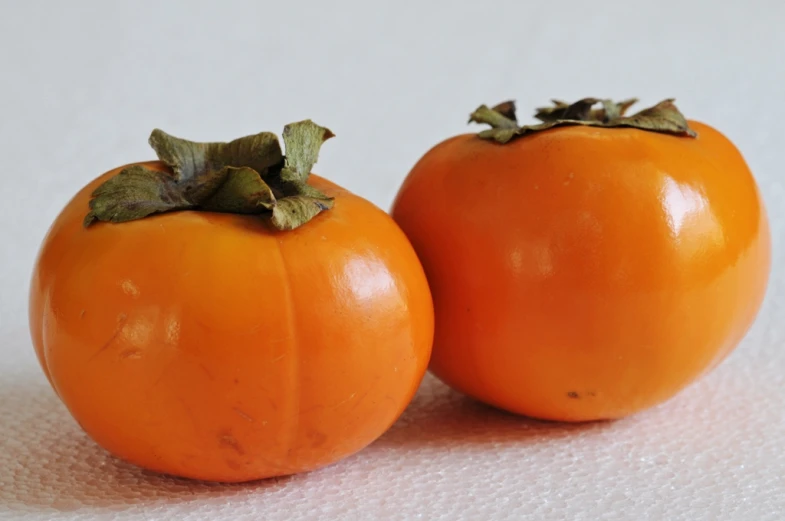 a pair of small orange tomatoes on a white table