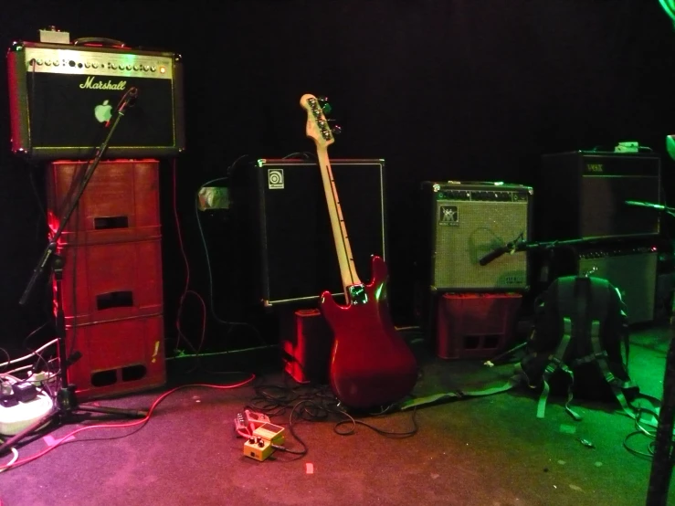 two guitars and two amps sit on the floor in front of a black wall