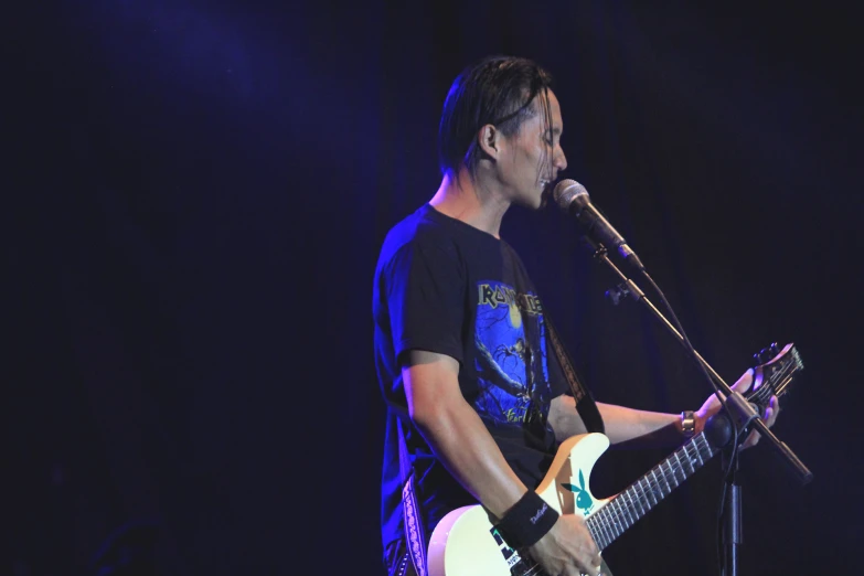 man playing guitar in front of microphone with dark background