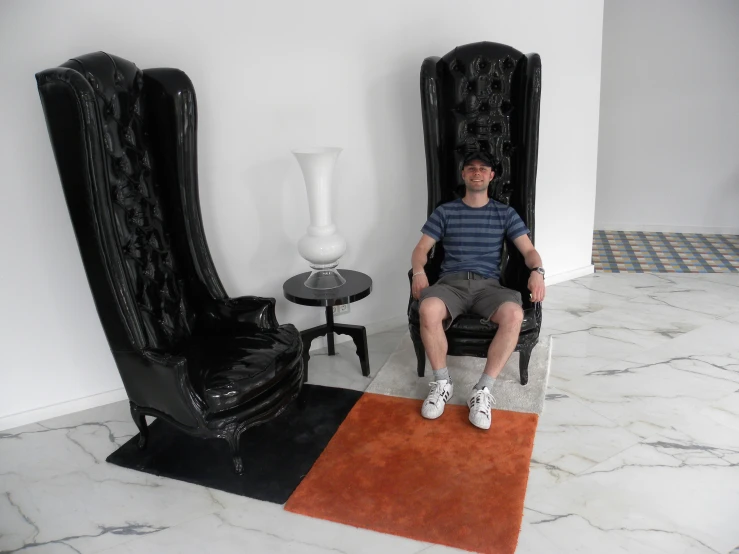 man sitting on black chair with one foot on rug near a table and chairs