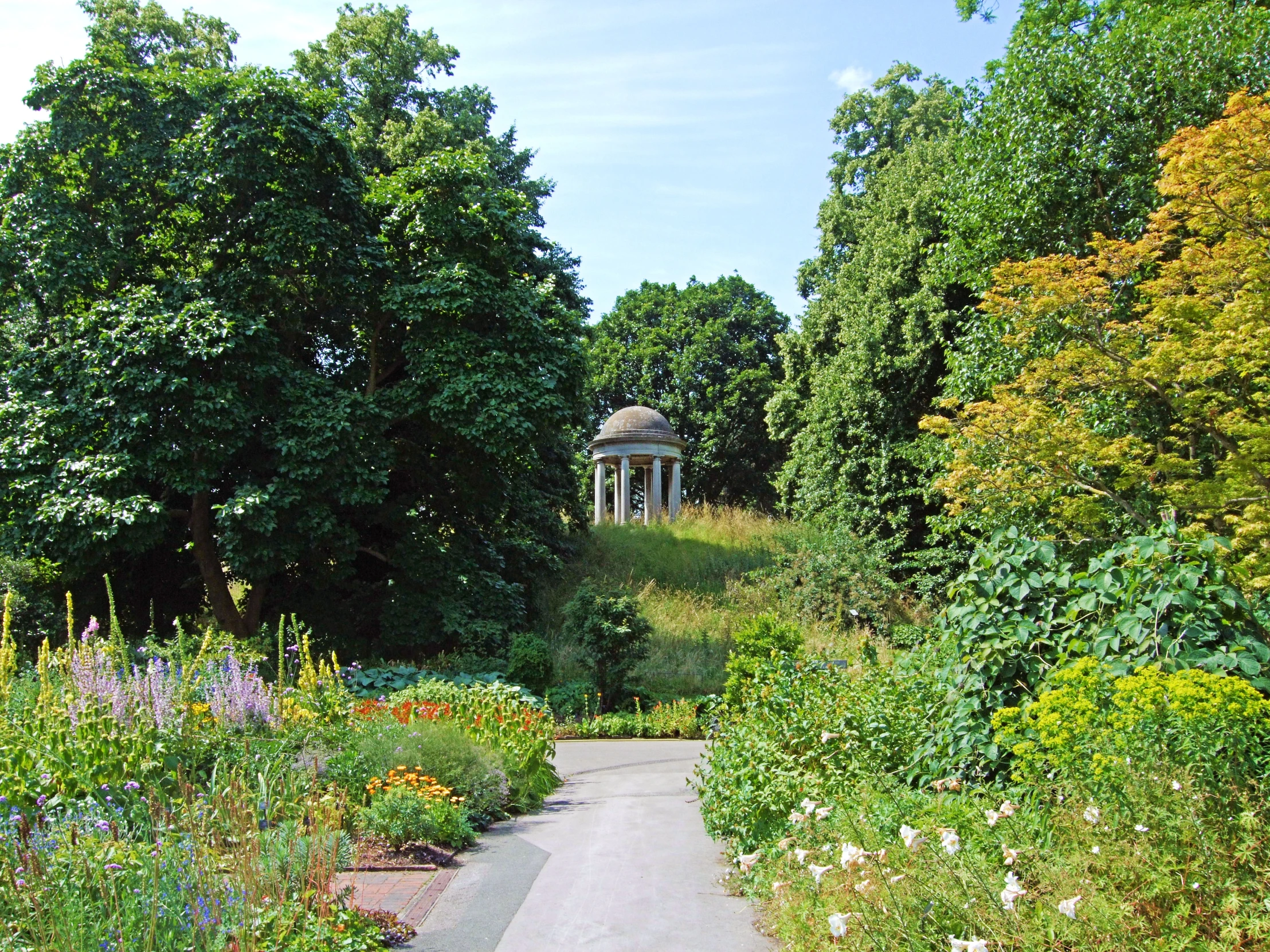 a road that leads through a forest and has a gazebo in the distance