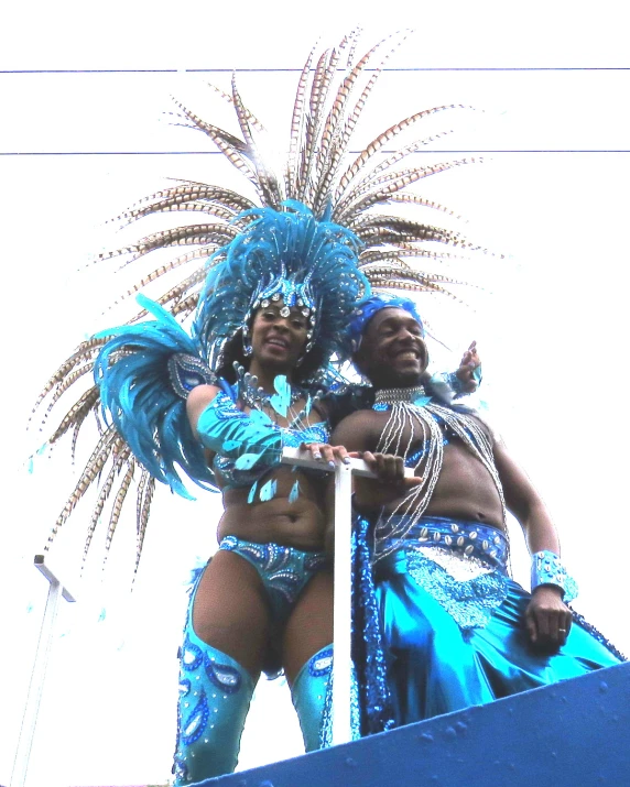 two women in elaborate costume pose on the top of a blue float