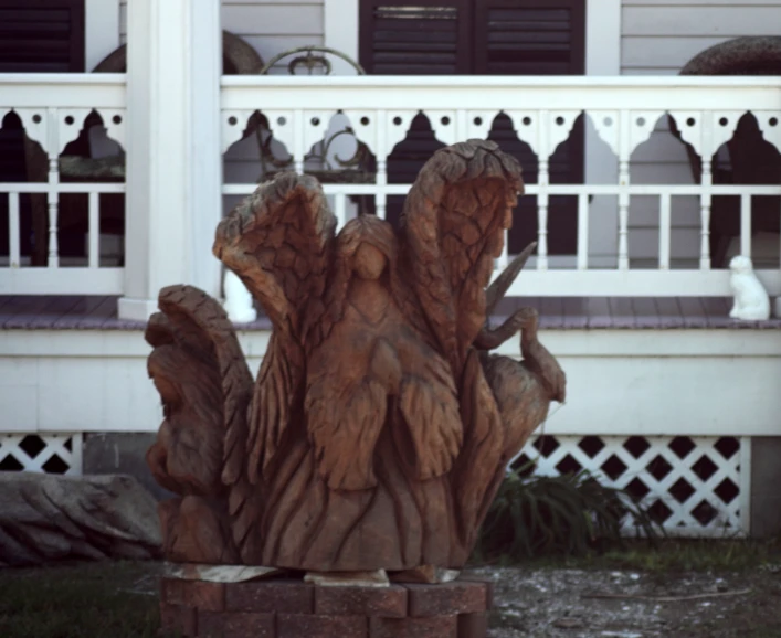 a wooden carving is on a lawn by some bushes