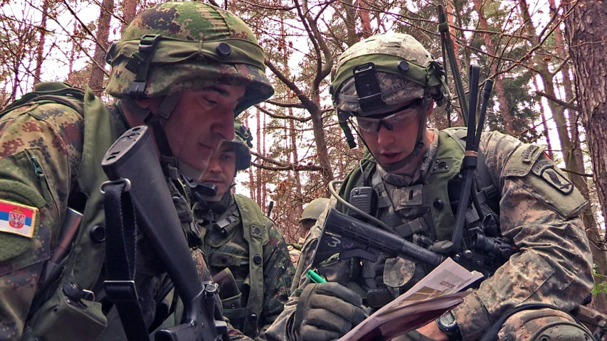 two soldiers sitting in the woods looking at soing in their hands