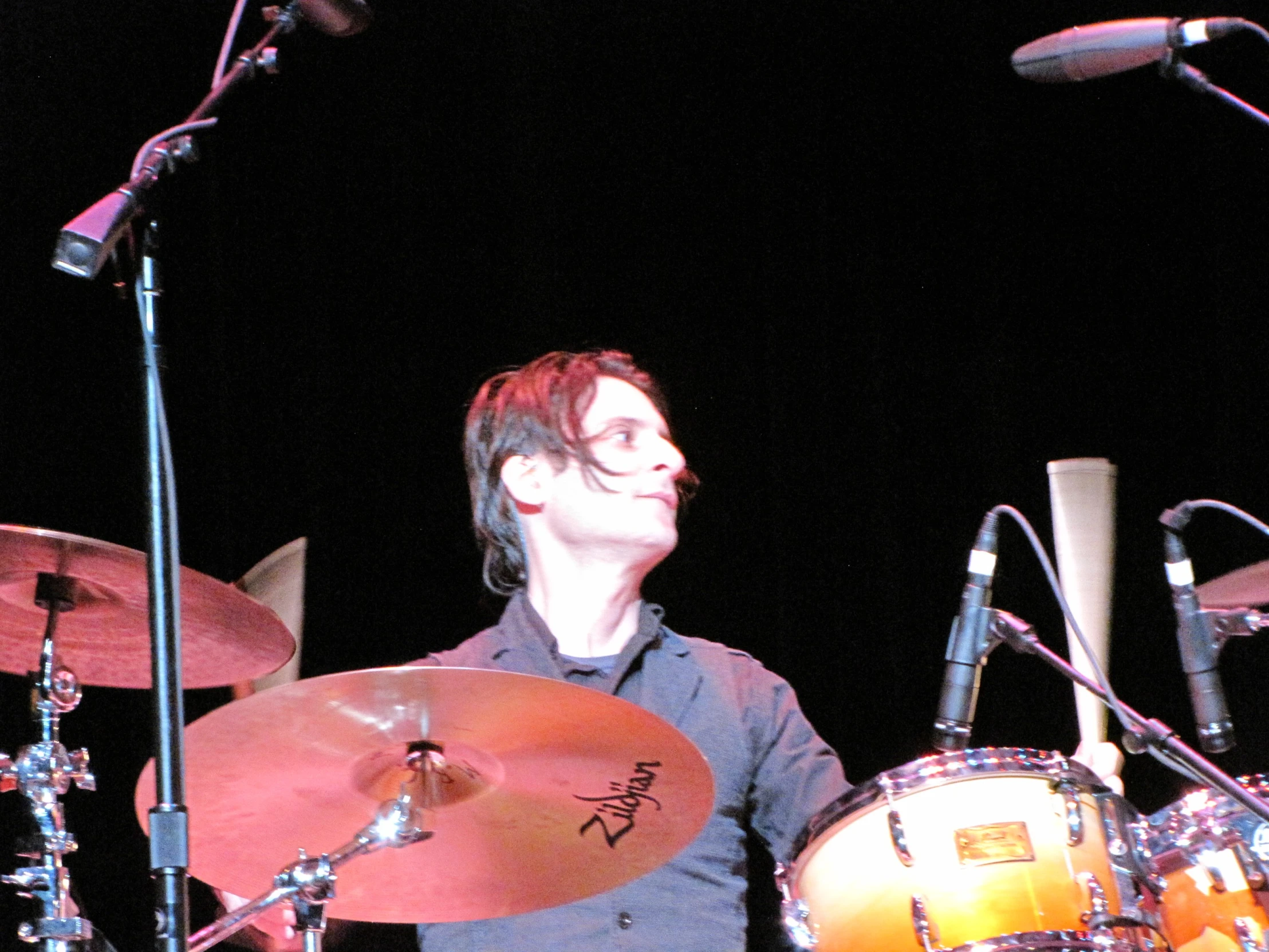 the drummer stands next to the drums in front of a microphone