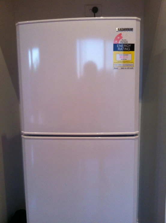 an upright, white fridge sits in the corner of a room