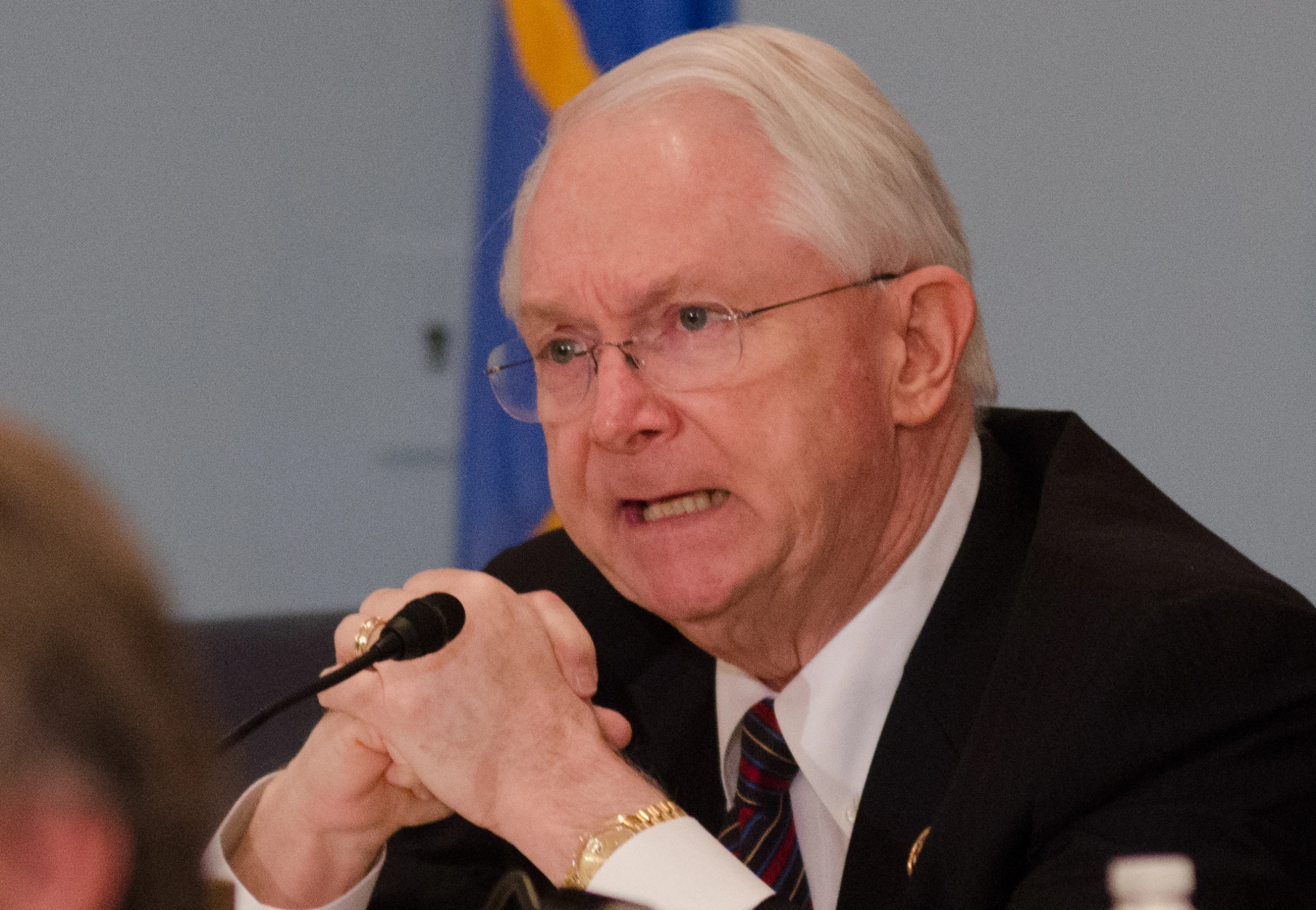 an older man wearing glasses speaking into a microphone