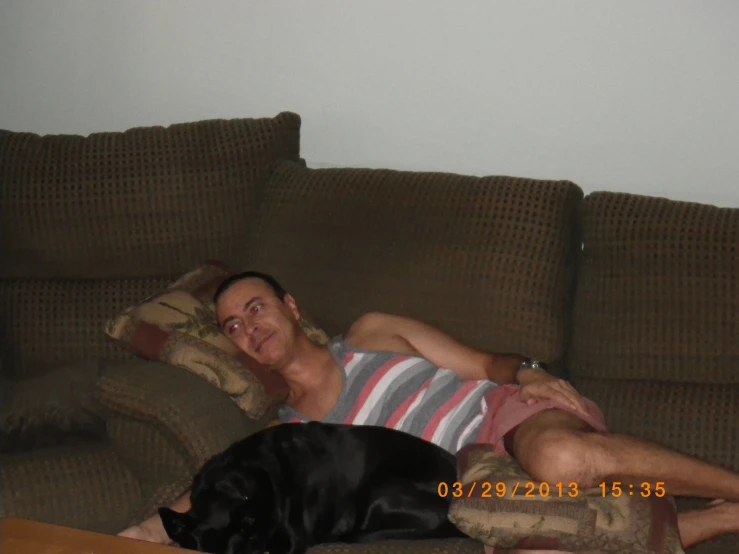 a man with his eyes closed sleeps on a couch next to a black dog