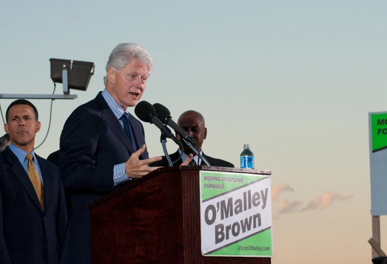 bill clinton speaks while other men stand behind him