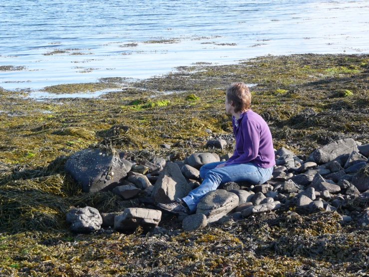 woman sitting on the rocks and staring out to water