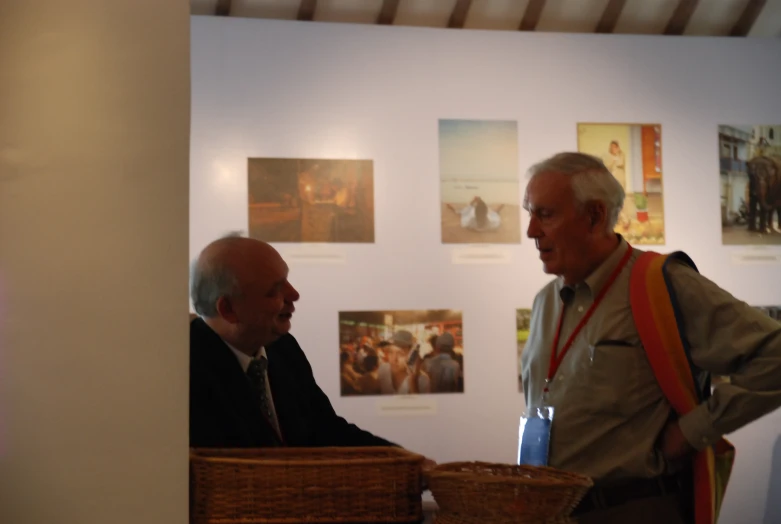 two men, one in an orange tie and one wearing a suit, meet in front of art work on display