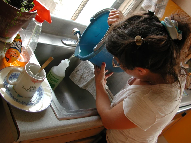 the young child is cleaning her dishes in the sink