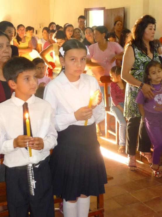 two boys in school uniforms standing next to each other holding lit candles