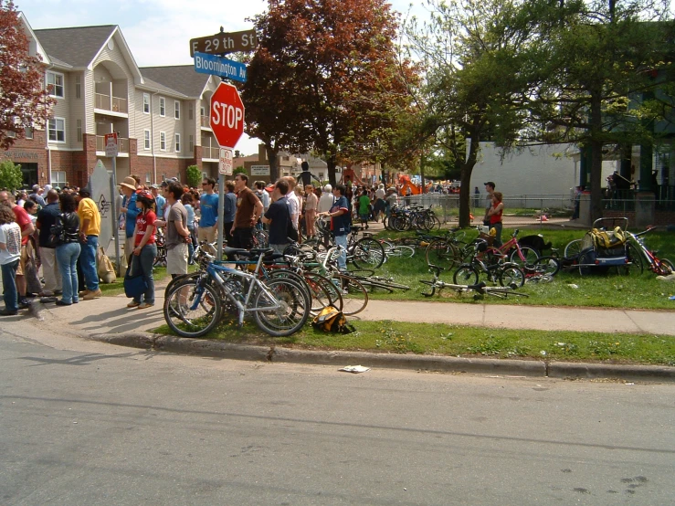 many people standing in the yard watching several bikes on the street