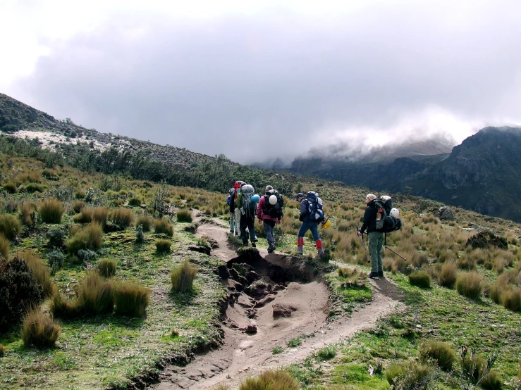 people with backpacks climbing up a hill on a cloudy day