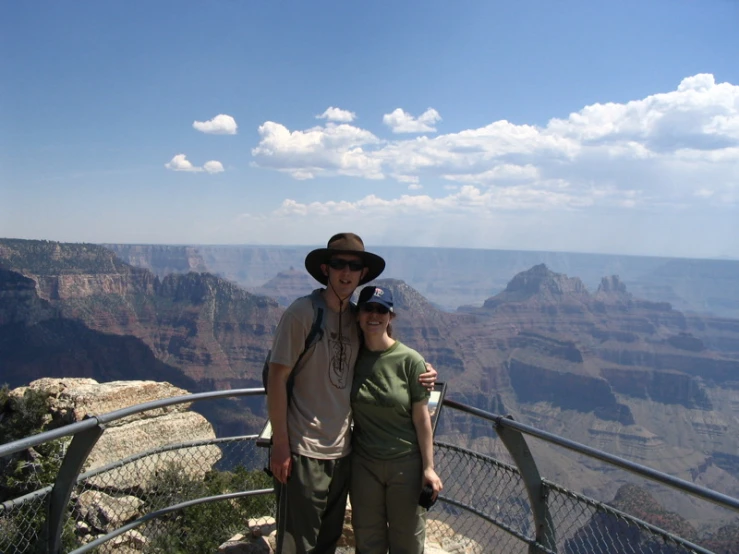 the man and woman are standing on the edge of the overlook with the canyon in the background