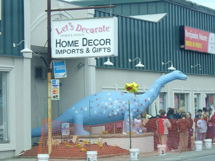 people gather outside a restaurant where there is a giant blue dinosaur sculpture