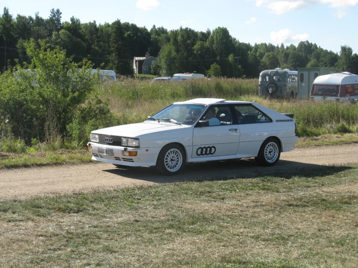 an old white car parked on the side of a dirt road