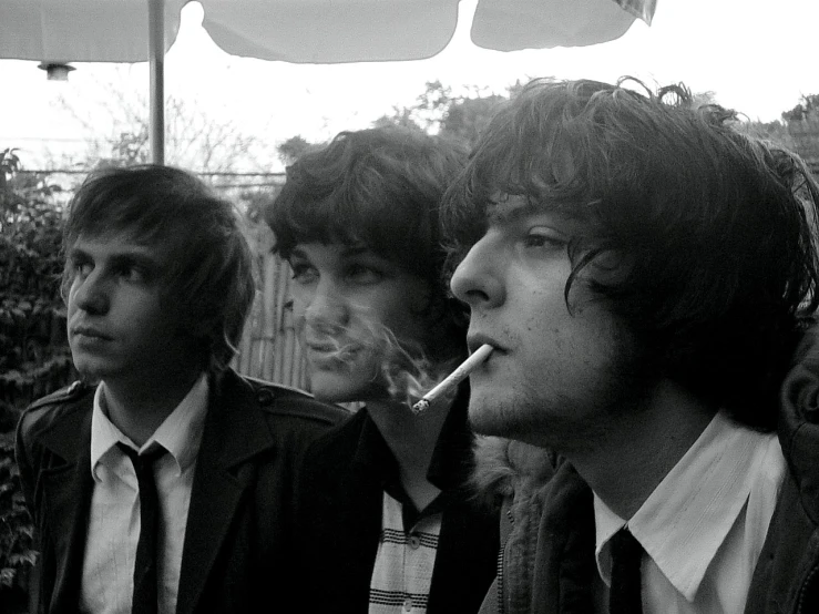 three men smoking and looking to one another