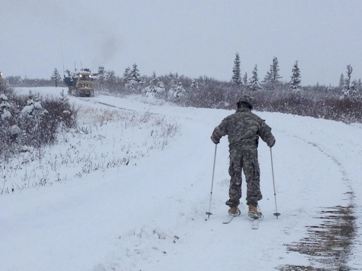 a soldier skiing down a snowy path with two vehicles