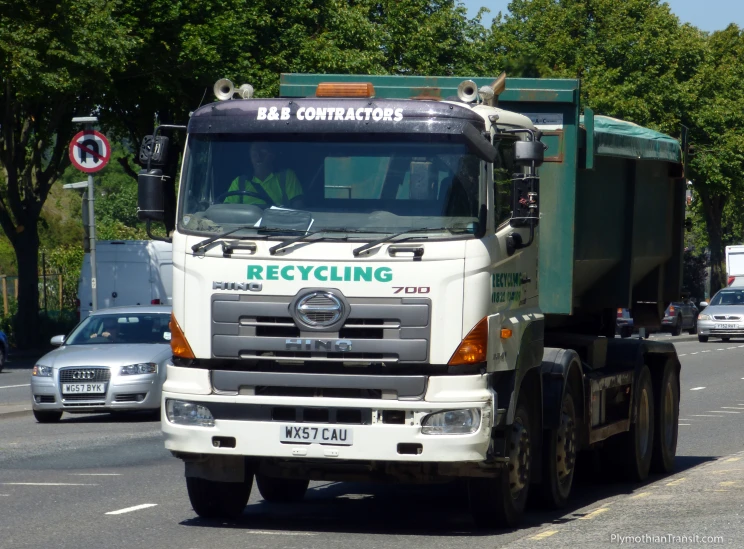 a green truck driving down a street next to a forest