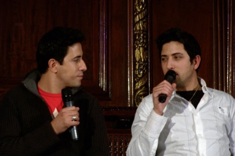 two young men standing next to each other in front of wooden walls