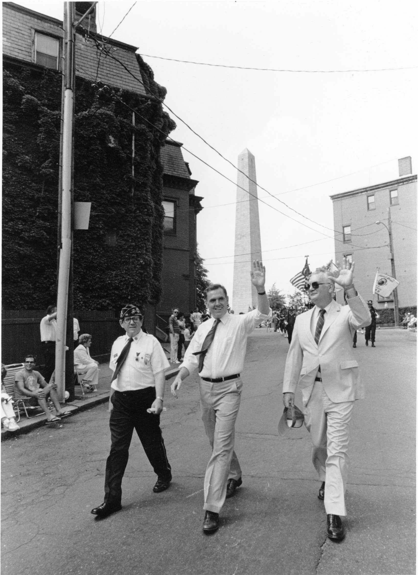 a black and white image of men in white suits walking down the street