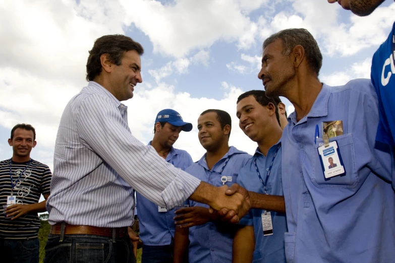 two men shake hands, with some other men behind them