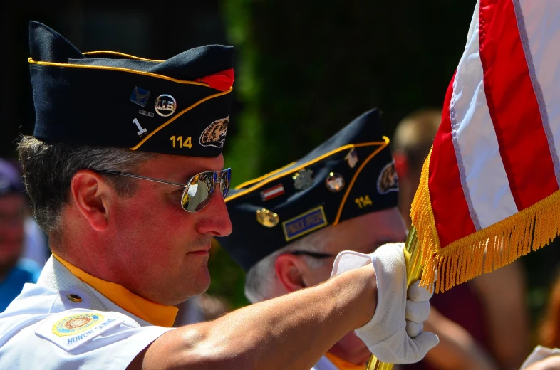 a man in uniform places a flag on top of another man's hat