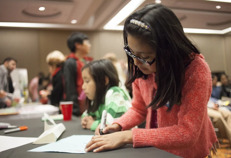 a  writing on a piece of paper while others look on