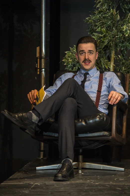 a man sits on a chair wearing a tie and a backpack