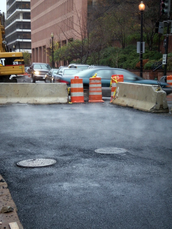 wet pavement next to street with traffic cones and buildings in background