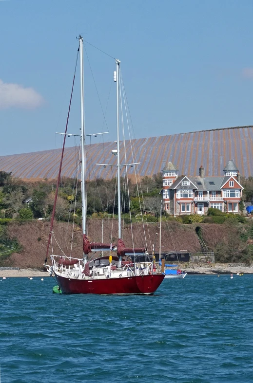 a sailboat in the water near a building on a hillside