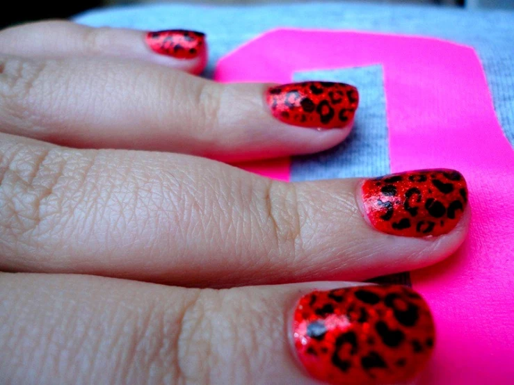 someone has their nails painted with red and black leopard print
