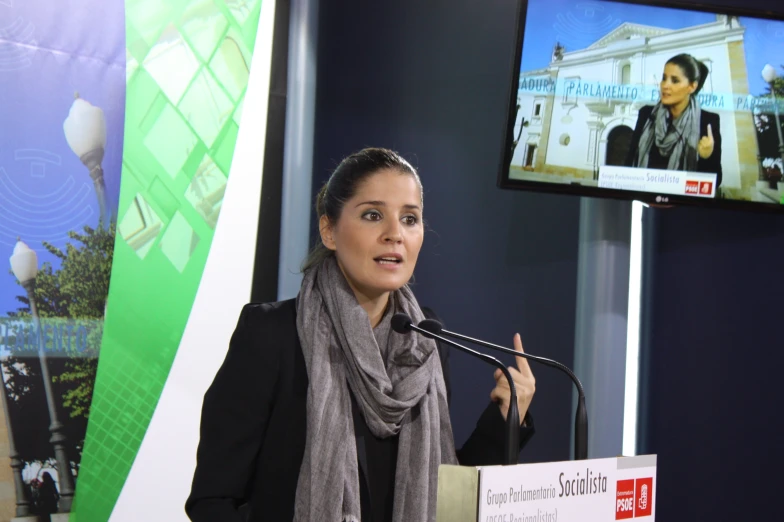 a woman giving a presentation at a podium in front of televisions