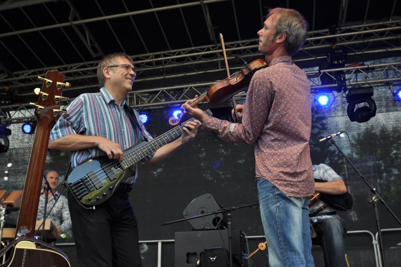 two men play instruments on the stage while another man sings