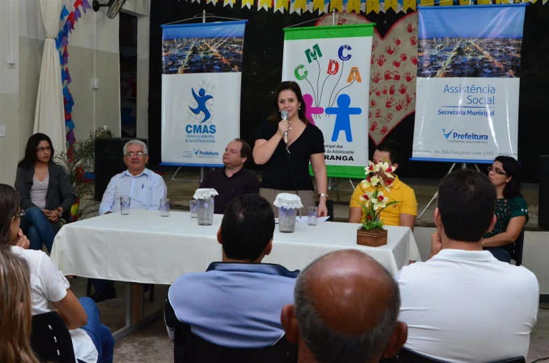 some people sitting at a table and a lady is giving a presentation