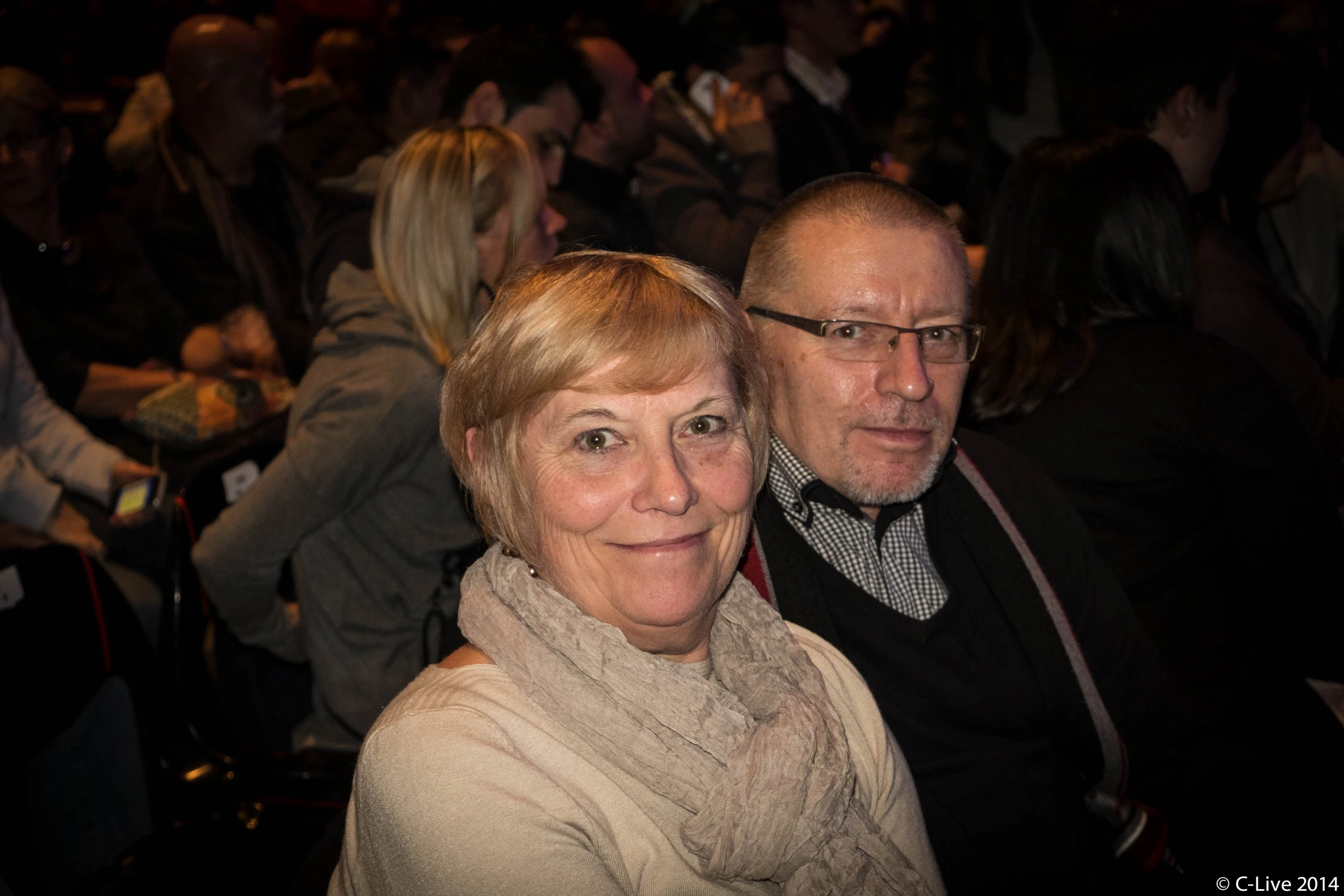 an older couple sitting side by side in front of a crowd