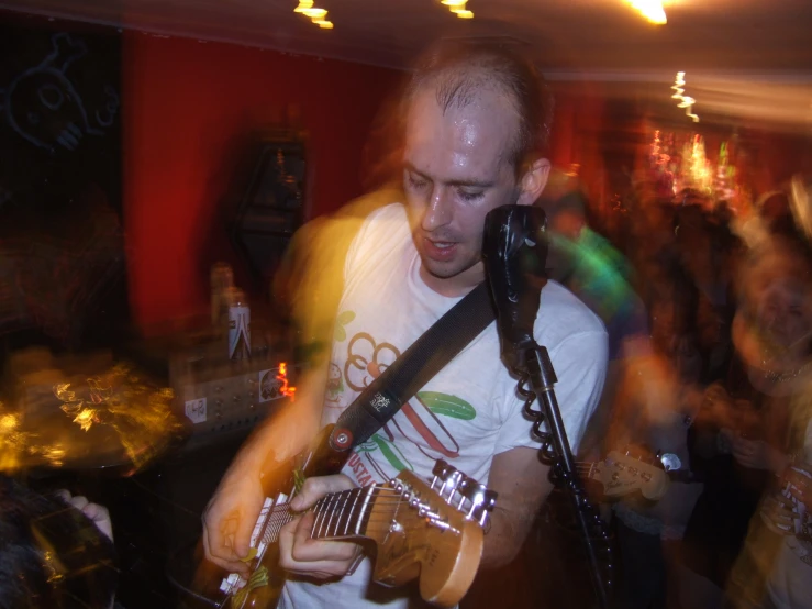 a man playing a guitar while standing in a room full of people