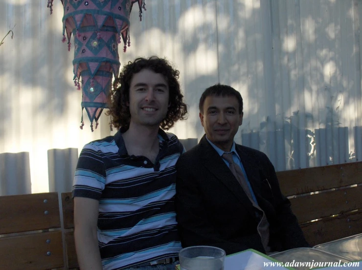 a man in a striped shirt sitting next to a man with a drink on a table