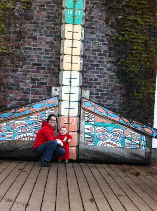 two people and an infant sit on a wooden floor by a wall with a painting on it