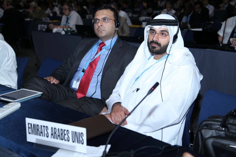 two men sitting at a table wearing suits and ties