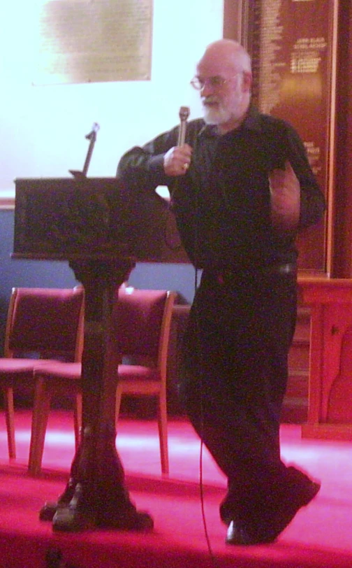 a man in black clothes standing at a podium holding a microphone