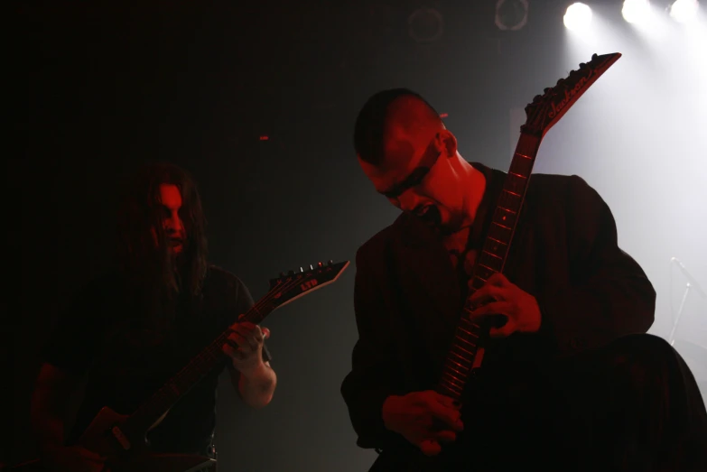 two people with guitars stand against spotlights on stage