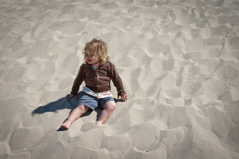 the young child is sitting on the sand